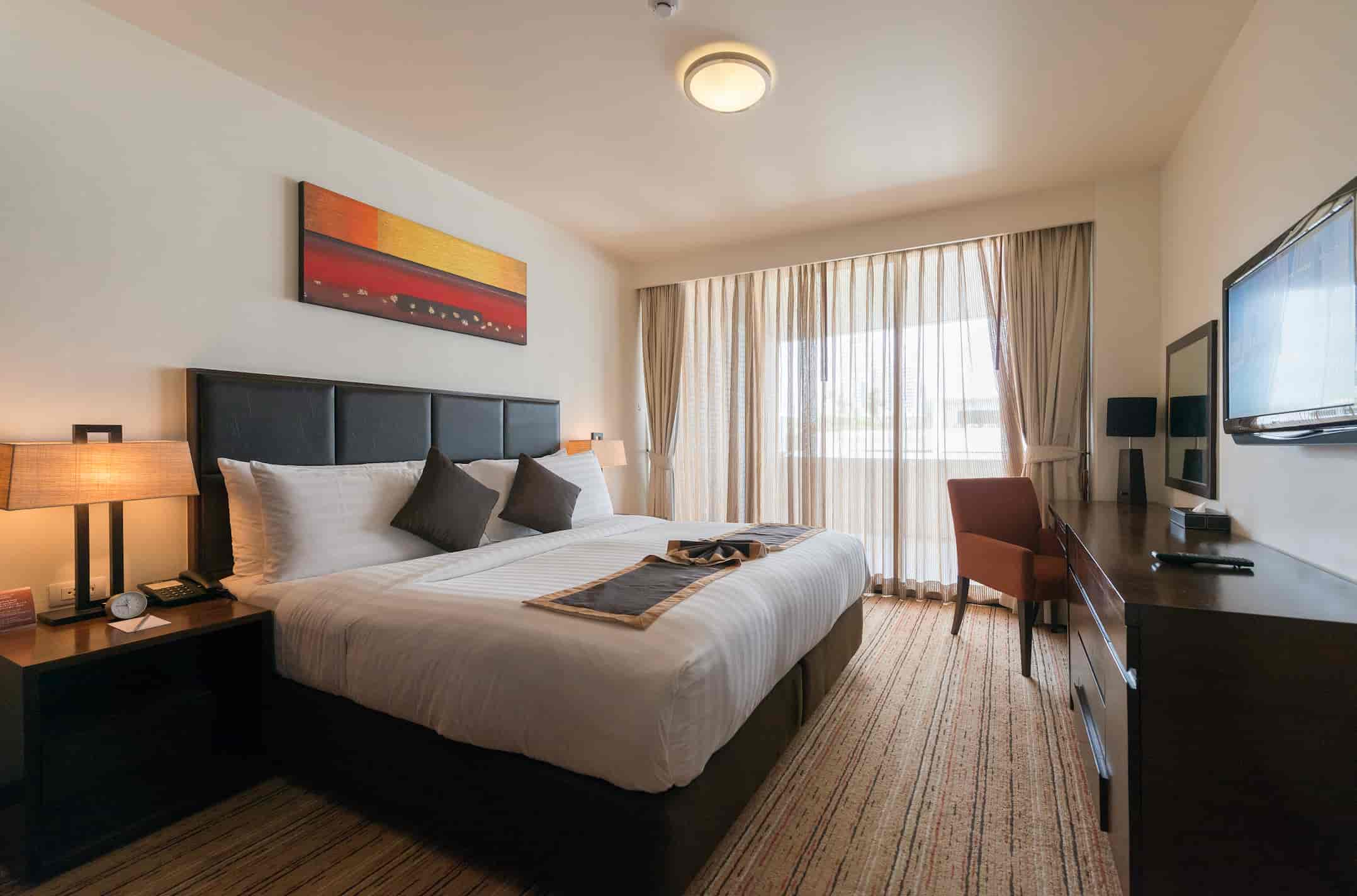 Guest room furniture manufacturer in Turkey presenting modern hotel bedroom with upholstered bed, desk, TV unit and curtains.