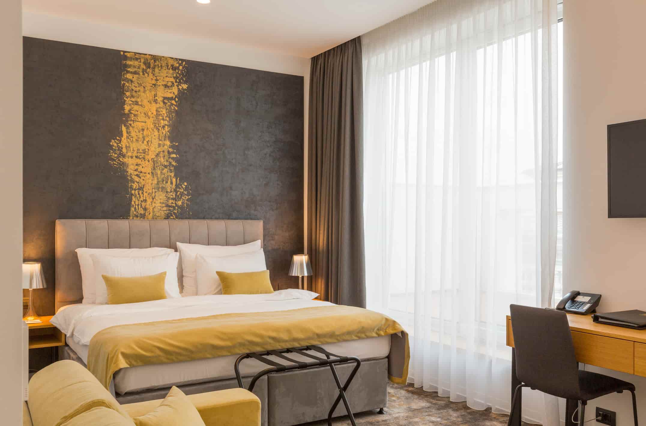 “Guest room furniture manufacturer in Turkey displaying modern hotel bedroom with upholstered bed, desk, armchair and custom lighting.